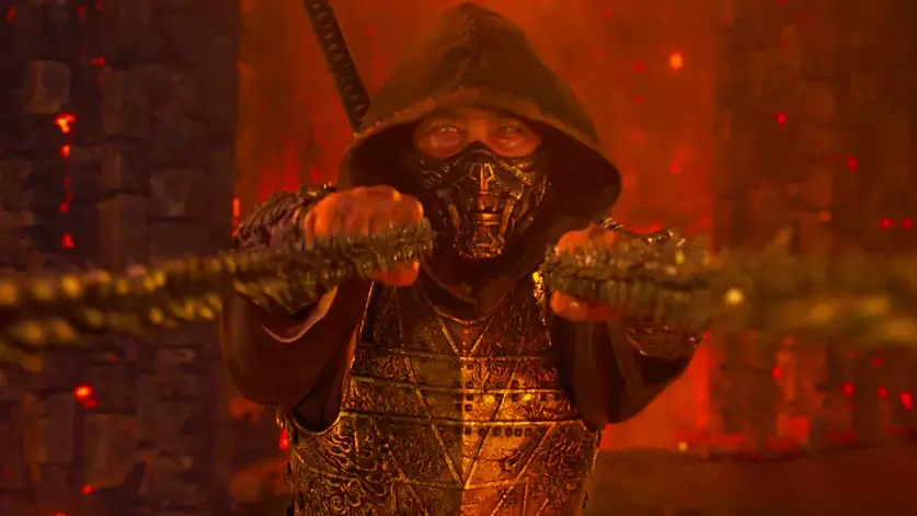 Scorpion de Mortal Kombat 2 segura correntes em cenário iluminado por fogo e tons alaranjados.